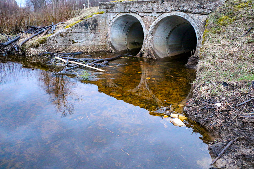 drainage pipes made of concrete under the road, to divert water during the spring flood. A strong stream of a forest stream, after a spring flood of a river, flows through concrete drainage pipes.