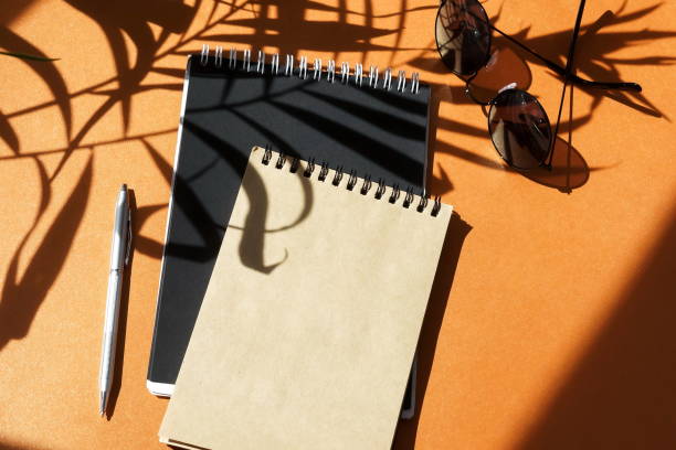 istock Open notebooks mock up, pen, sunglasses  and floral shadows on orange background. copy space 1225316156