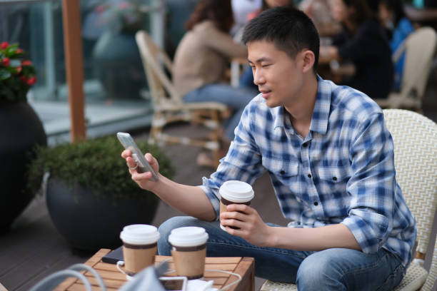 istock close up one young Asian man using phone at outdoor cafe. 1225316939