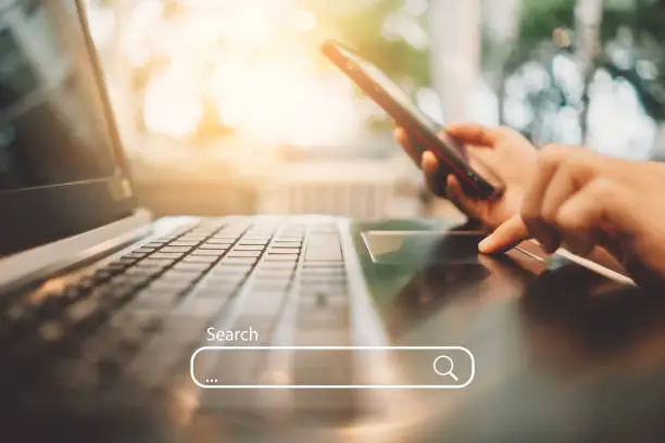 Woman hand using keyboard laptop with search bar icon on screen at coffee shop. Business technology and freelance concept. Vintage tone filter effect color style.