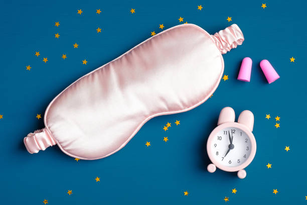 istock Healthy sleeping concept. Sleep eye mask, alarm clock, ear plugs on dark blue background. Flat lay, top view. 1225324645