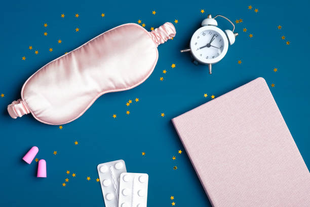 istock Flat lay composition with sleep eye mask, alarm clock, dream book, sleeping pills for insomnia, pink ear plugs on dark blue background. Sleep hygiene, healthy sleeping, insomnia treatment concept 1225324652