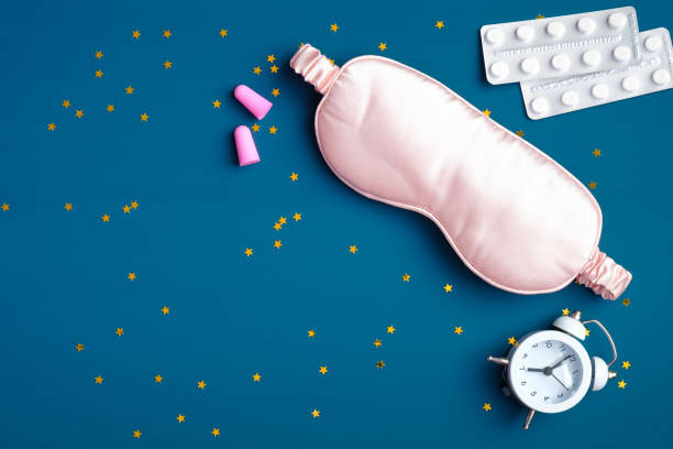 istock Flat lay composition with pink sleep eye mask, alarm clock, ear plugs, sleeping pills for insomnia on dark blue background with confetti. Sleep hygiene, insomnia treatment concept 1225324654