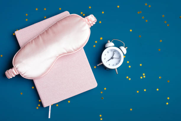 istock Good night and healthy sleeping concept. Top view sleeping accessories on dark blue background. Flat lay composition with sleep eye mask, pink dream book, alarm clock, confetti. Insomnia treatment. 1225324660