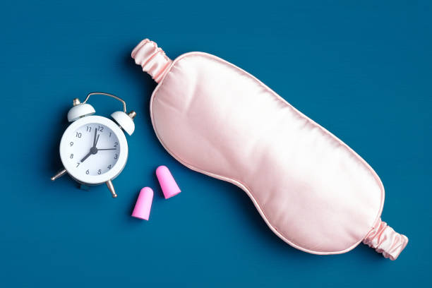 istock Sleep eye mask with alarm clock and ear plugs on dark blue background. Sleeping accessories for good night, sleeping routine, insomnia treatment concept. Flat lay, top view. 1225324661