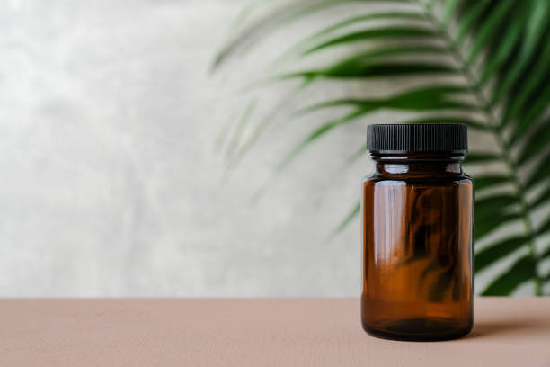 Clear empty pill bottle with tropical leaf. Transparent medicine bottle of brown glass mockup. Clear empty pill bottle with tropical leaf. Transparent medicine bottle of brown glass mockup. pharma herbal medicine pill medicine stock pictures, royalty-free photos & images