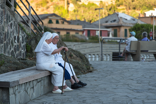 Bonassola, Liguria / Italy - August 24, 2016: two nuns sitting on a bench on the promenade by the sea, resting and enjoying the conversation in the early evening