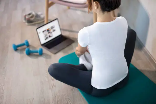 Young slim woman at home training. Workout online with a laptop. and fitness mat. Online training, online fitness, stay home, quarantine, online training. Stretching training. Online sport lessons.