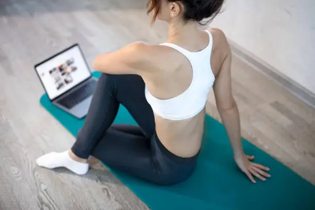 Young slim girl at home training. Workout online with a laptop. and fitness mat. Online training, online fitness, stay home, quarantine, online training. Stretching training. Online sport lessons.