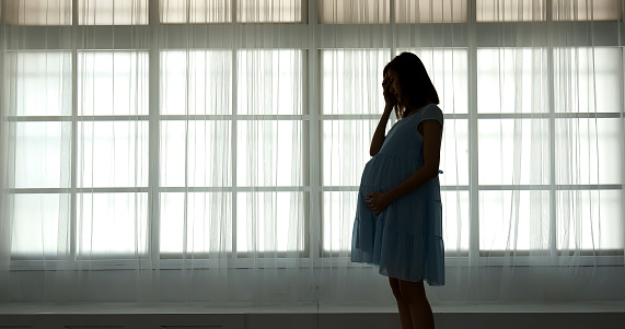 pregnant woman feel depression standing in front of window