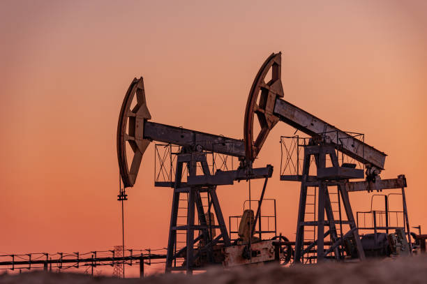 equipo de bomba de aceite. producción de petróleo y gas. sitio de yacimientos petrolíferos. pump jack está funcionando. perforación de rricks para la producción de combustibles fósiles y la producción de petróleo crudo. guerra contra los precios d - wellhead fotografías e imágenes de stock