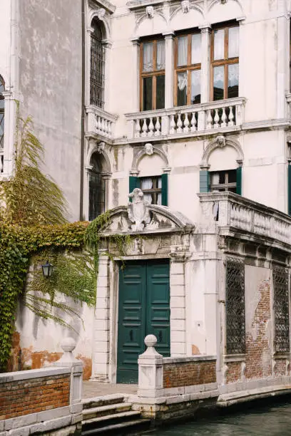 Photo of Beautiful stone arched entrance to the building, a green door and classic Venetian windows. Details of building facades on the streets of Venice, Italy.