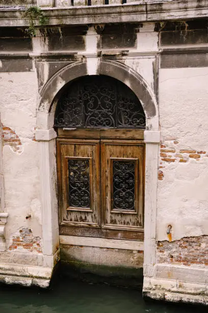 Photo of Closeup of the facade of a building, on the streets of Venice, Italy. Entrance from the water to the building. Antique wooden door with wrought metal patterns.