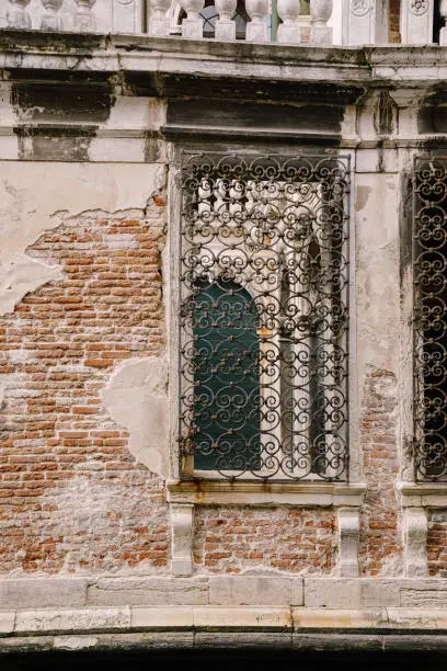 Photo of Closeup of the facade of a building, on the streets of Venice, Italy. Stone wall texture and wrought iron metal grill.