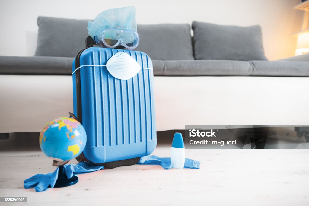 Travel bag suitcase with earth globe, gloves, mask and head protection from viruses and flu influenza. Tourist traveling canceled all over the world, 2020. season is postponed. Anxiety Stock Photo