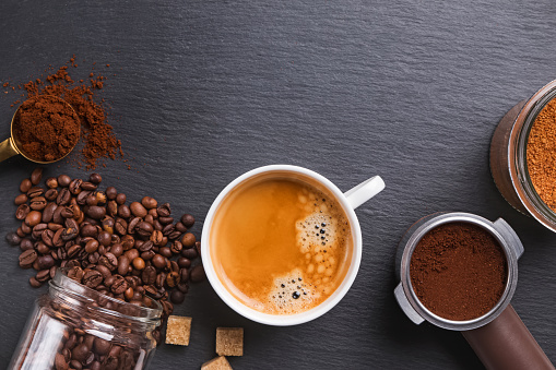 Top view of cup of Espresso, coffee beans, ground and sugar on black stone table.