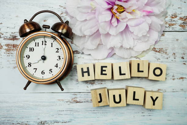 istock Hello July with alarm clock on wooden background 1225345866