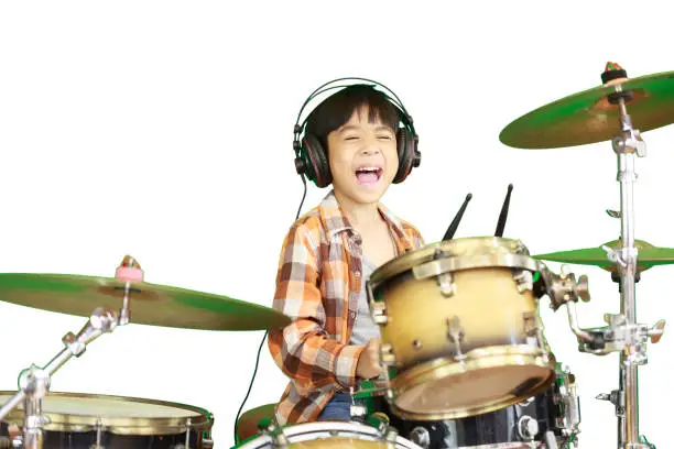 Photo of A cute Asian boy is enjoying playing the drums in a music classroom.
