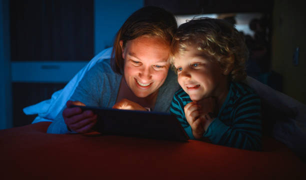istock Cute blond boy and his mother using digital tablet at bedtime 1225348411