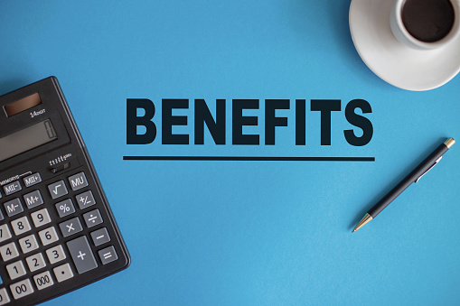 The word BENEFITS is written on a blue background next to a calculator, pen, and coffee Cup