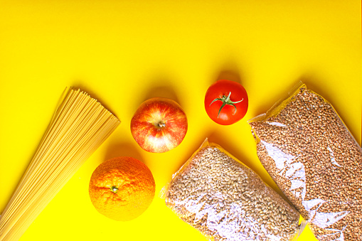Food supplies for quarantine on yellow background. Pasta, vegetables, fruits, cereals.