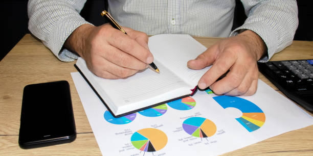 istock A man writes in a diary. On a wooden table are charts, a phone, a calculator. 1225362352