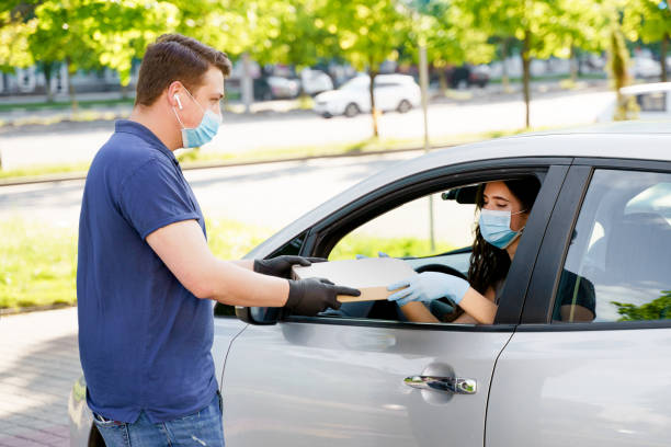 mensajero de entrega de alimentos da pizza a la mujer en coche ecológico. alimentos de seguridad entregados según la distancia social. pizza sabrosa con salami, queso, tomates en caja de cardoard. dar comida por la ventana del auto. - cardoard fotografías e imágenes de stock