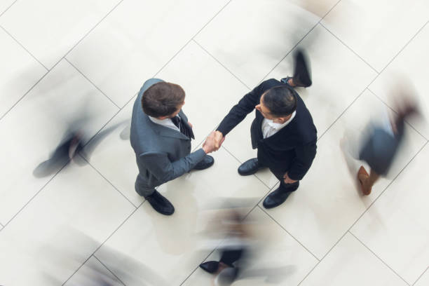 Business handshake in crowd Business people shaking hands standing in a crowd of walking people, top view defocused office business motion stock pictures, royalty-free photos & images