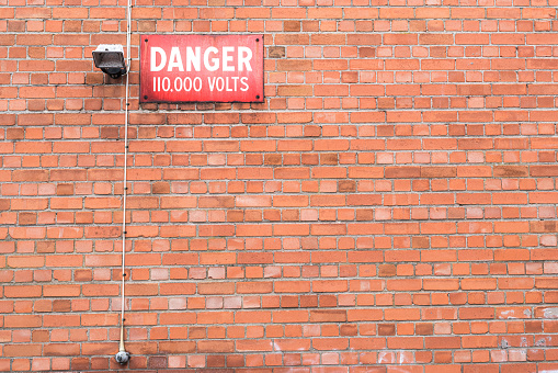 Sign attached to a brick wall, warning of a high voltage industrial electricity transformer.  Belfast, Northern Ireland.