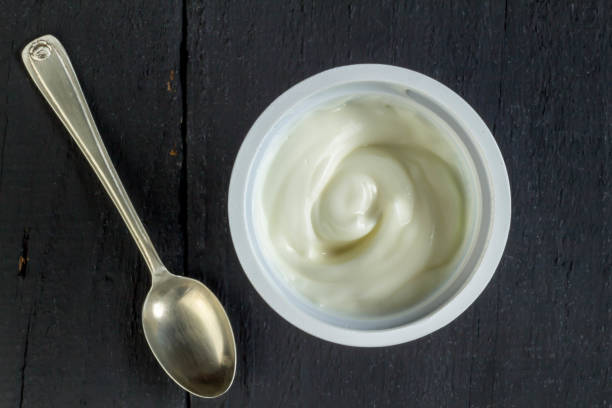 istock natural organic white yogurt, Greek yogurt, plastic cup with white yoghurt on black background - overhead photo 1225387908