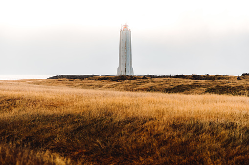 Dramatic view of beautiful big white lighthouse surrounded by the golden meadow on West Iceland