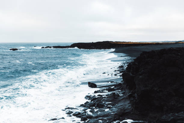 Scenic view of the beautiful black beach, rock cliffs and moody wavy ocean at the West Iceland