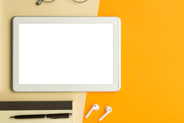 istock Flat lay, top view of orange office table desk with tablet computer screen mockup with clipping path and wireless earphones, notebook, glasses, pen 1225390508