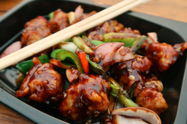 image du repas épicé de poulet de kung pao de poulet dans le récipient jetable en plastique noir avec des baguettes en bois, l’oignon, les poivrons rouges et verts, vue surélevée - pao photos et images de collection