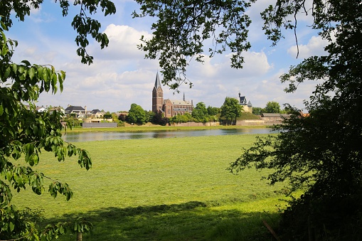 View from Beesel over green agriculture field and river Maas with boat on medieval church and castle of Kessel - Netherlands