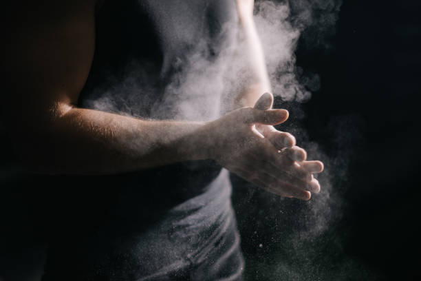 Close-up of unrecognizable muscular man clapping hands with talc and preparing for workout at gym. Close-up of unrecognizable muscular man clapping hands with talc and preparing for workout at gym. Closeup of athletic male hands preparing for fit workout in gym with chalk magnesium carbonate. sports chalk stock pictures, royalty-free photos & images