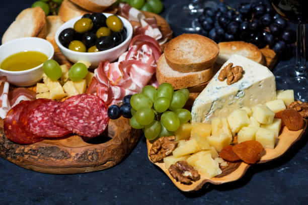 istock cheese platter on a wooden board, bread, fruit and cold cuts on dark background, closeup 1225398558