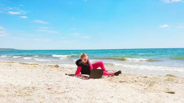 Girl on the seashore with a laptop. Rest, happiness, nature, distant work.