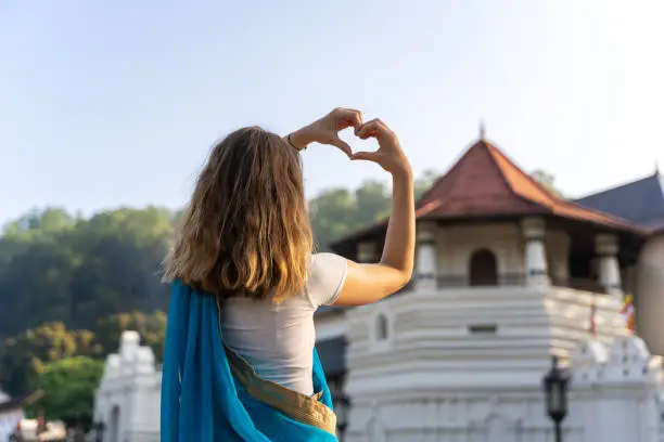 Photo of young caucasian woman is making heart with her finger in front of Sri Dalada Maligwa temple