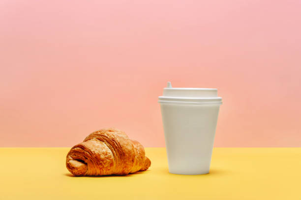 istock Croissant and a white cup for coffee or tea on a yellow-pink background. 1225406082