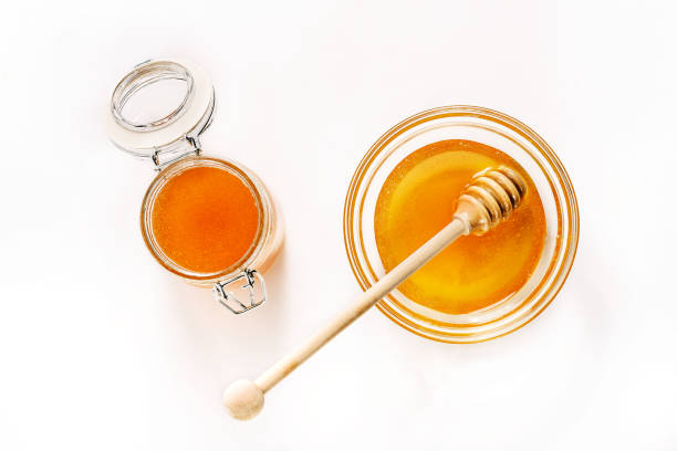 glas und untertasse mit honig und einem löffel für honig isoliert auf weißem hintergrund. - syrup jar sticky isolated objects stock-fotos und bilder