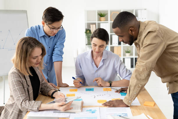 istock Four intercultural analysts on smart casualwear bending over table with papers 1225410100