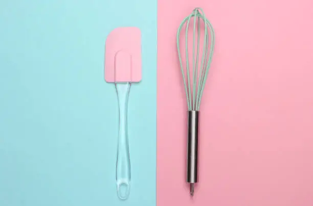 Kitchen spatula and whisk on pink blue pastel background. Minimalism. Top view