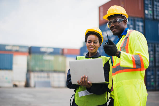 istock Young African american men and woman worker Check and control loading freight Containers by use computer laptop and radio at commercial shipping dock smiling felling happy. Cargo import export concept 1225414594