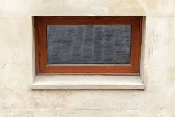 A small window of a basement in the glass of which a cobblestones are reflected.