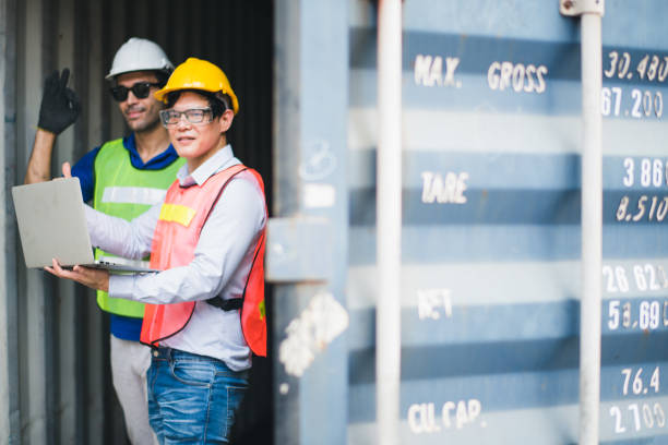 Young man worker and foreman Check and control loading freight Containers by use computer laptop at commercial shipping dock felling serious. Engineer inspection. Cargo freight ship import export. trabajador de joven y capataz compruebe y controle los contenedores de carga de carga mediante el uso de computadora portátil en el muelle de embarque comercial talión grave. inspección de ingenieros. exportación de importación de buques de carga de c