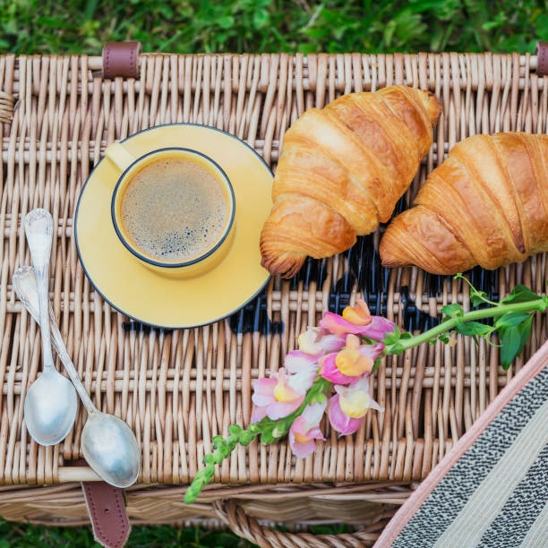 Two french croissants and cup of coffee on wicker basket.