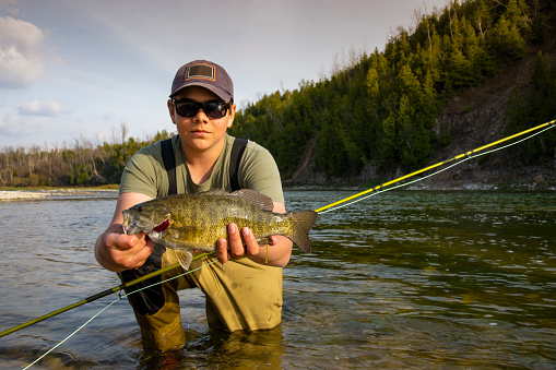 A teen fly-fisher holding a fish on a beautiful tributary river of the Lake Huron.  Real scenario.