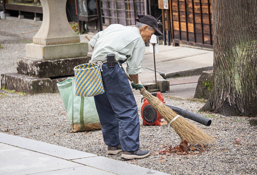 Takayama, Japan - November 18, 2019: Man sweeping leaves near Sakurayama Hachimangu Shrine.