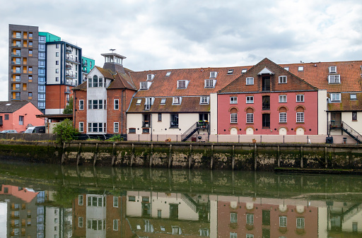 Seen from St Peter’s Dock in Ipswich, Suffolk, Eastern England, the former Stoke Bridge Maltings, now converted into a row of apartments. The building is beside Stoke Bridge, which crosses the River Orwell. The still water reflects the building with a green tinge.